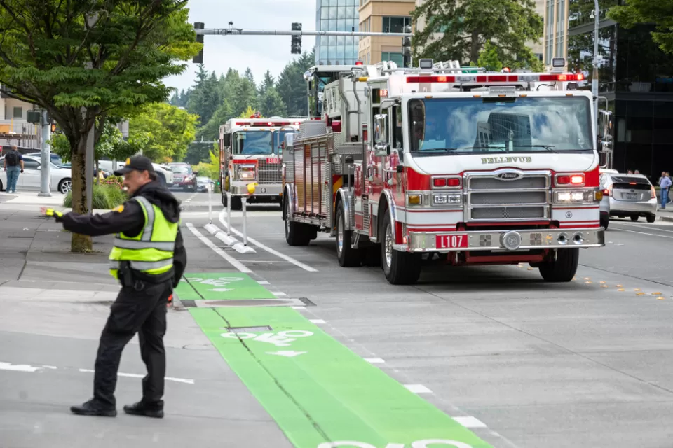 A police officer directs traffic as fire trucks arrive on scene along a street with green painted bike lanes.